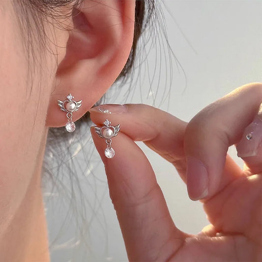 Close-up of a person wearing angel-shaped earrings with a blurred background
