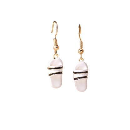 A pair of dangling earrings with white stone-like pendants featuring black stripes, suspended from gold fishhook wires, displayed on a beige jewelry stand.