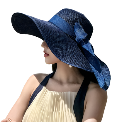 Woman wearing a blue sun hat with a bow, standing outdoors with greenery in the background.
