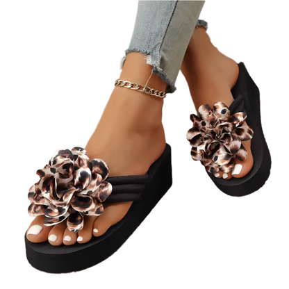 Black sandals with floral leopard print straps worn by a person on a textured floor.