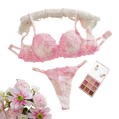 Pink lace lingerie set with flowers and makeup palette on a white surface