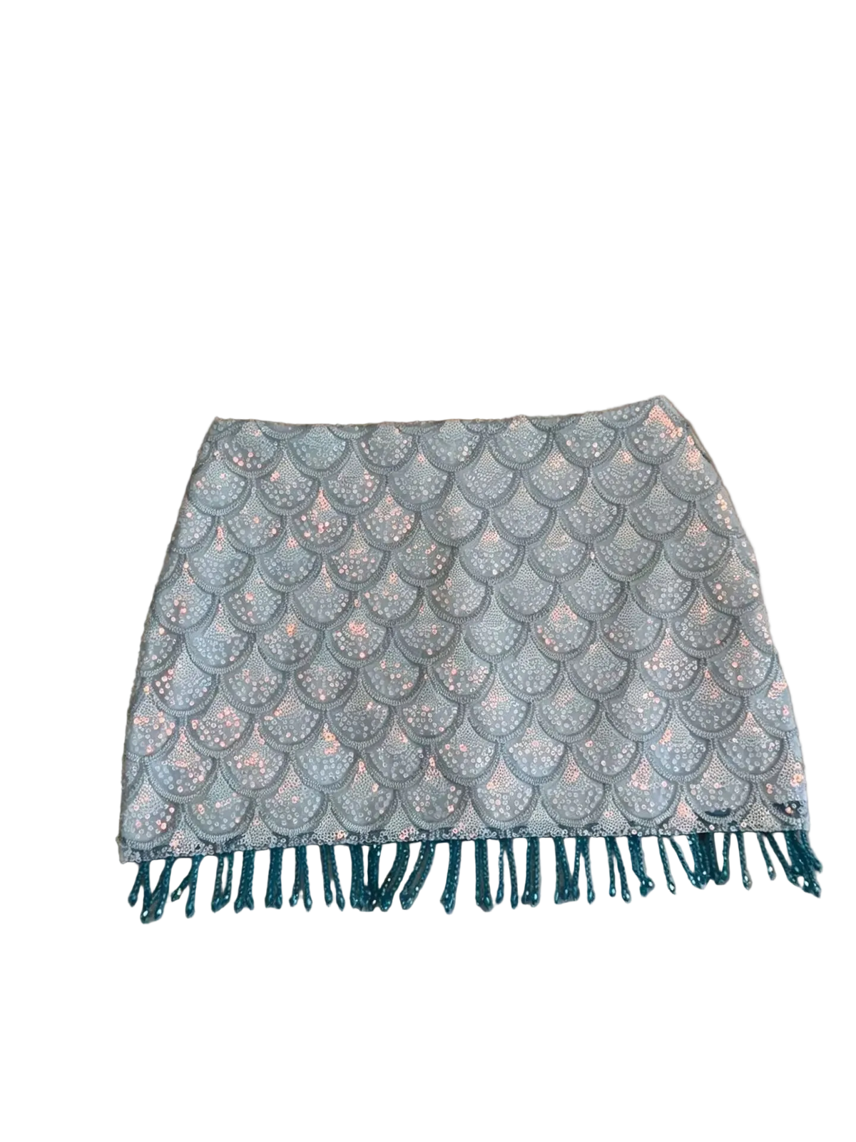 A light gray mini skirt with a scalloped mermaid-scale pattern and teal fringe, laid flat on a beige leather couch.