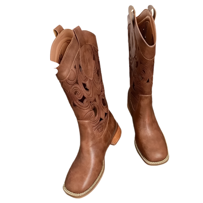 Brown cowboy boots with intricate designs on a wooden surface.
