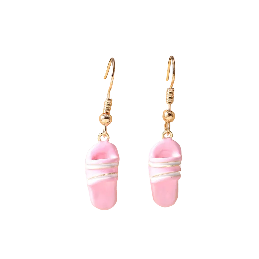 A pair of gold-tone dangle earrings with pink slipper-shaped charms wrapped in white wire, displayed on a beige ceramic stand.