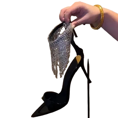 Black high-heeled shoe with sparkling embellishments held by a hand against a neutral background