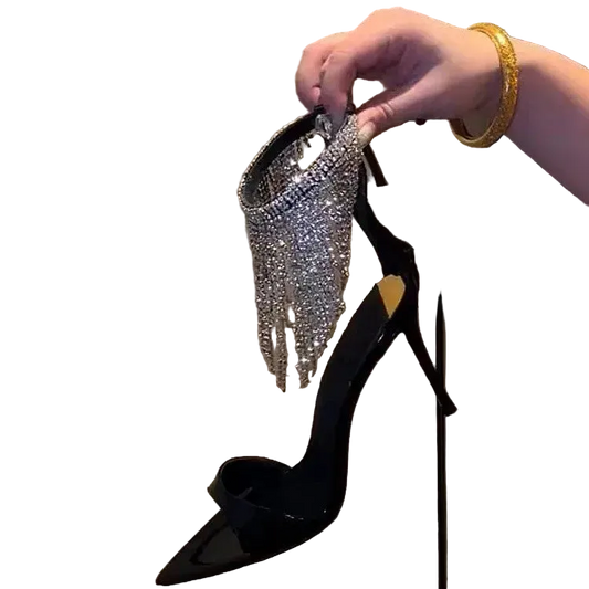 Black high-heeled shoe with sparkling embellishments held by a hand against a neutral background