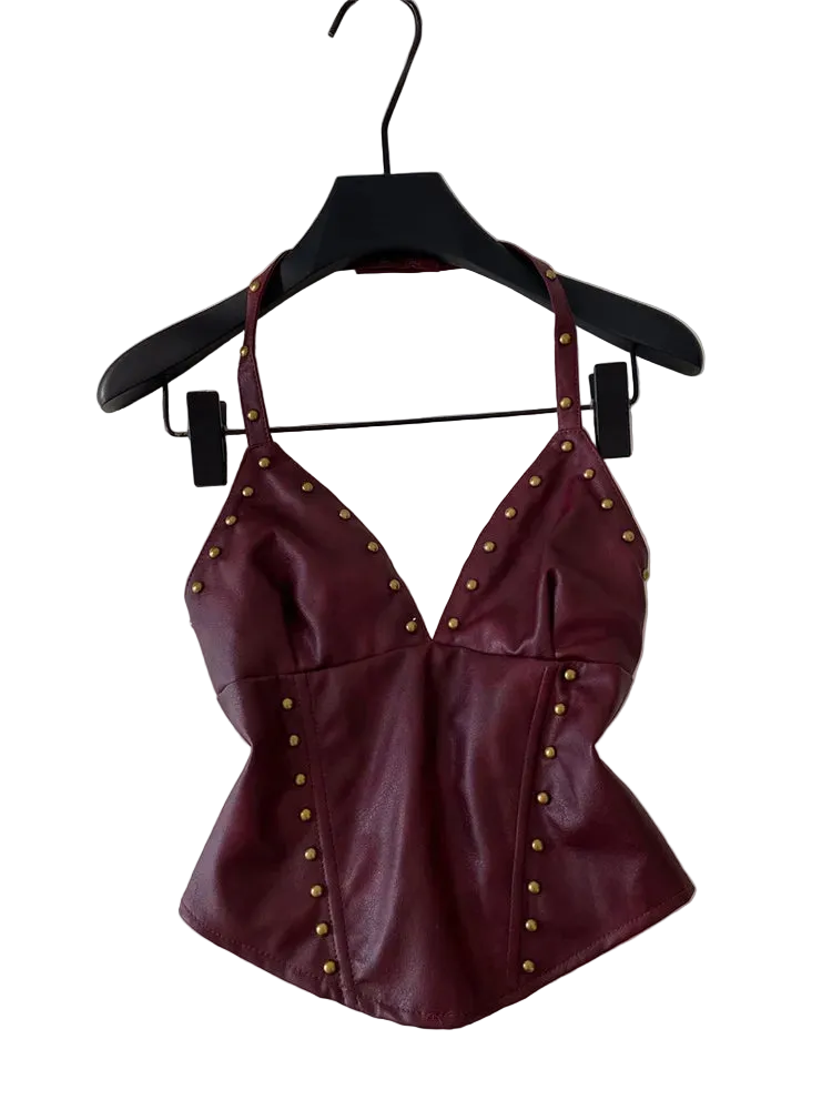 A burgundy faux leather halter top with gold-tone studs, hanging on a black hanger against a white wall.