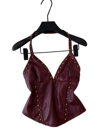 A burgundy faux leather halter top with gold-tone studs, hanging on a black hanger against a white wall.