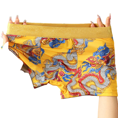 Yellow boxer briefs with dragon design held by hands on a gray background