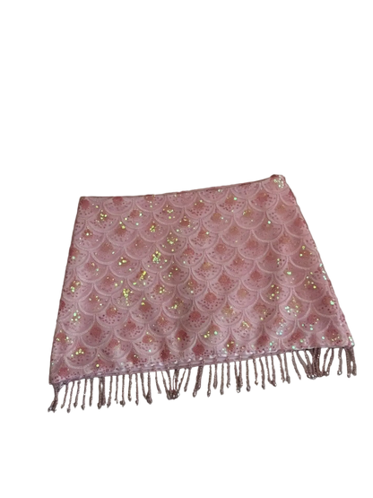 A pink sequined scarf with a scalloped lace pattern and fringe, laid flat on a beige leather sofa.