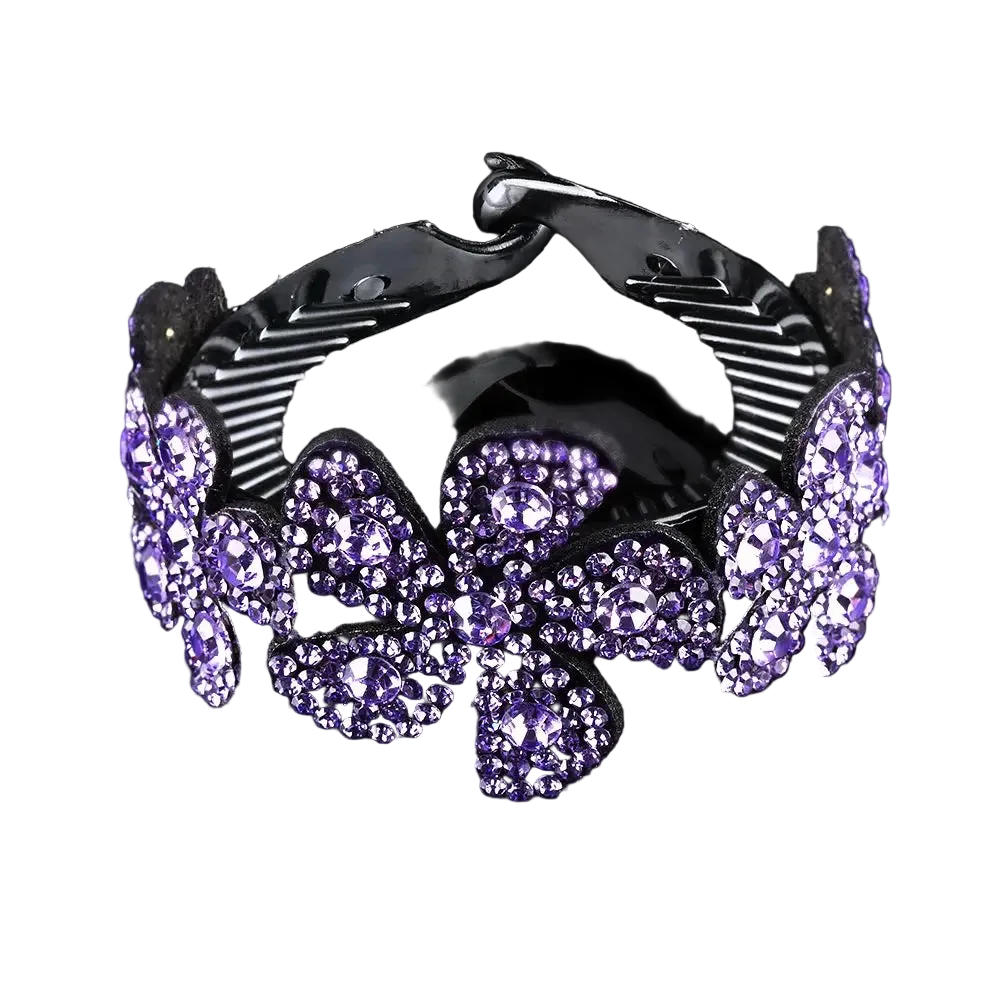 A black hair claw clip embellished with sparkling purple rhinestones in a floral pattern, shown on a reflective black background.