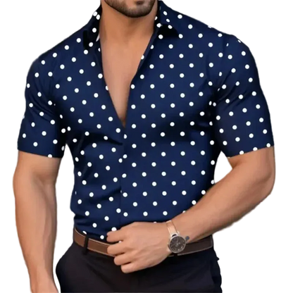 Man wearing a navy blue shirt with white polka dots, standing against a blurred background.