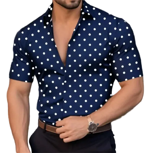 Man wearing a navy blue shirt with white polka dots, standing against a blurred background.
