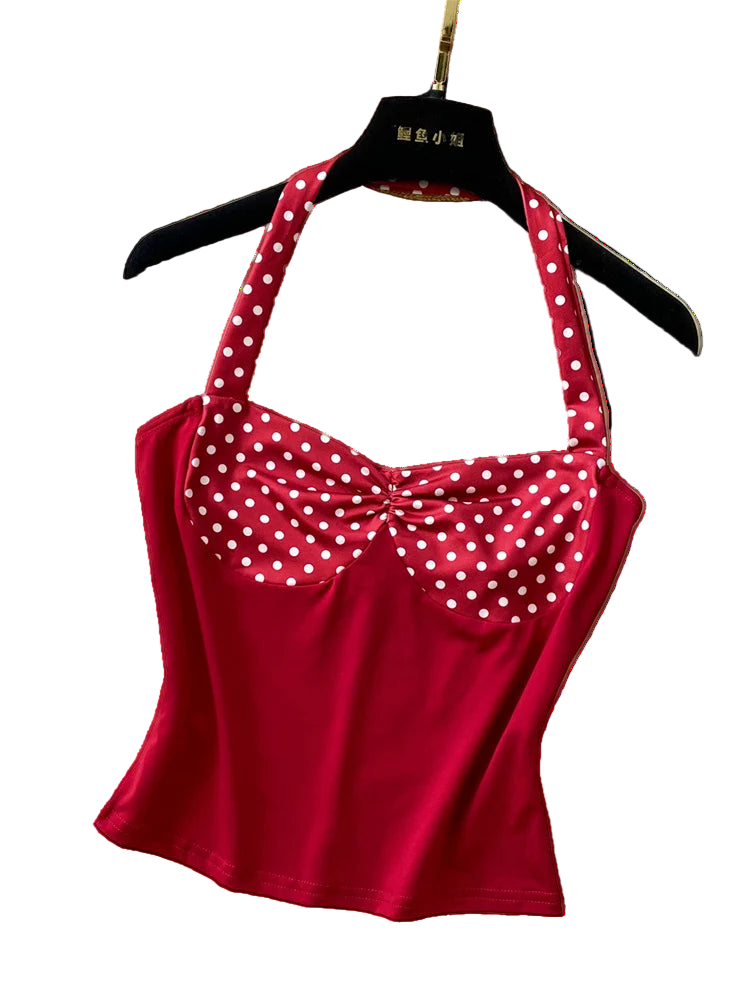 Red polka dot top on a hanger with a hat and necklace on a textured surface