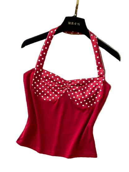 Red polka dot top on a hanger with a hat and necklace on a textured surface