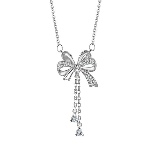 A silver bow pendant necklace adorned with small clear crystals, featuring a delicate chain and two dangling crystal charms, shown on a plain white background.