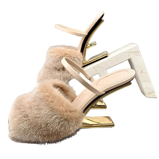 Beige fur slide sandal with gold heel on a reflective surface