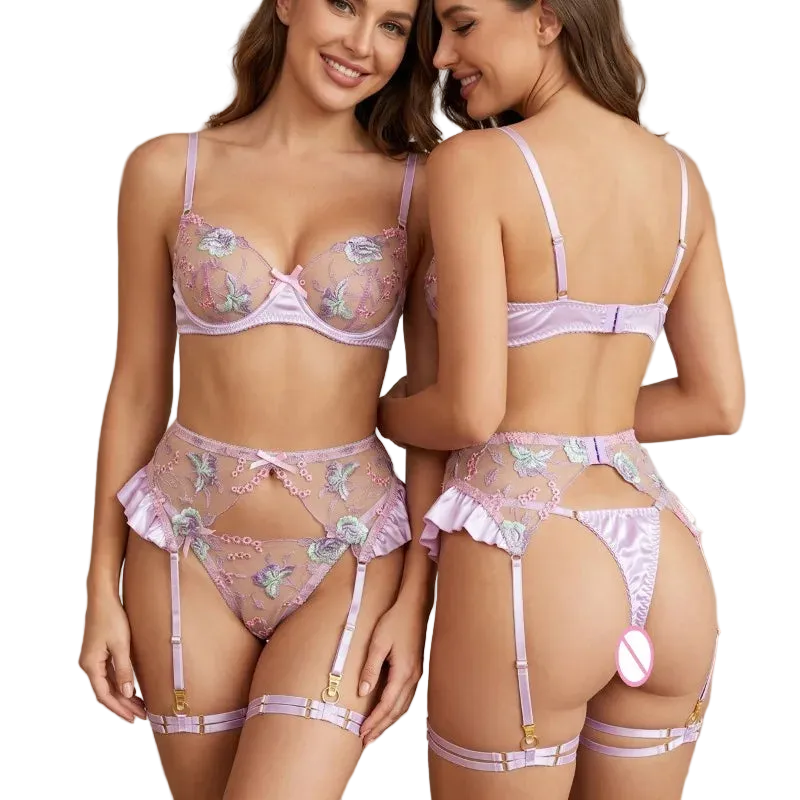 Two models wearing a light purple/lavender floral lingerie set, shown from both the front and back. The set includes a sheer mesh bra with embroidered flowers, matching high-waisted briefs, a thong, and garter straps with gold-tone hardware.