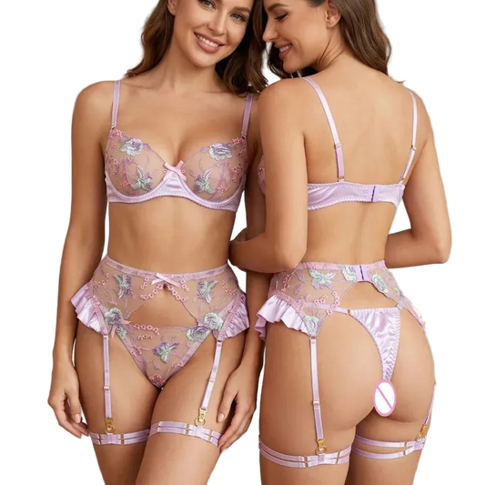 Two models wearing a light purple/lavender floral lingerie set, shown from both the front and back. The set includes a sheer mesh bra with embroidered flowers, matching high-waisted briefs, a thong, and garter straps with gold-tone hardware.